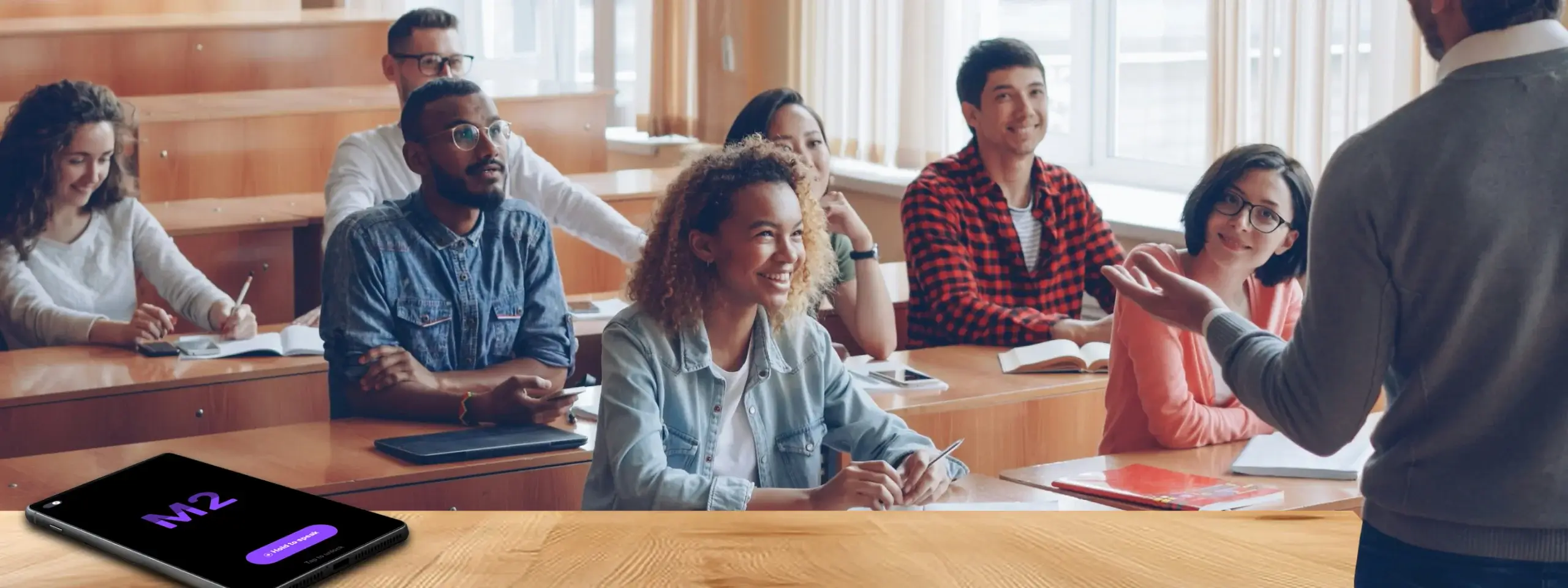 Teacher leading an engaged classroom discussion while students participate attentively, with a tablet showing the M2talk participation interface in the foreground.
