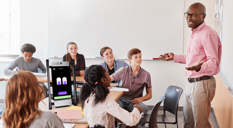 M2 at the front of a classroom guiding a whole-group activity as a teacher engages students in discussion