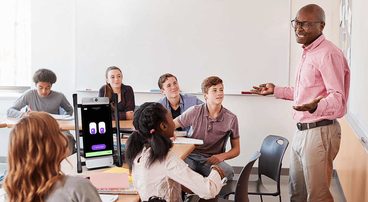 M2 at the front of a classroom guiding a whole-group activity as a teacher engages students in discussion