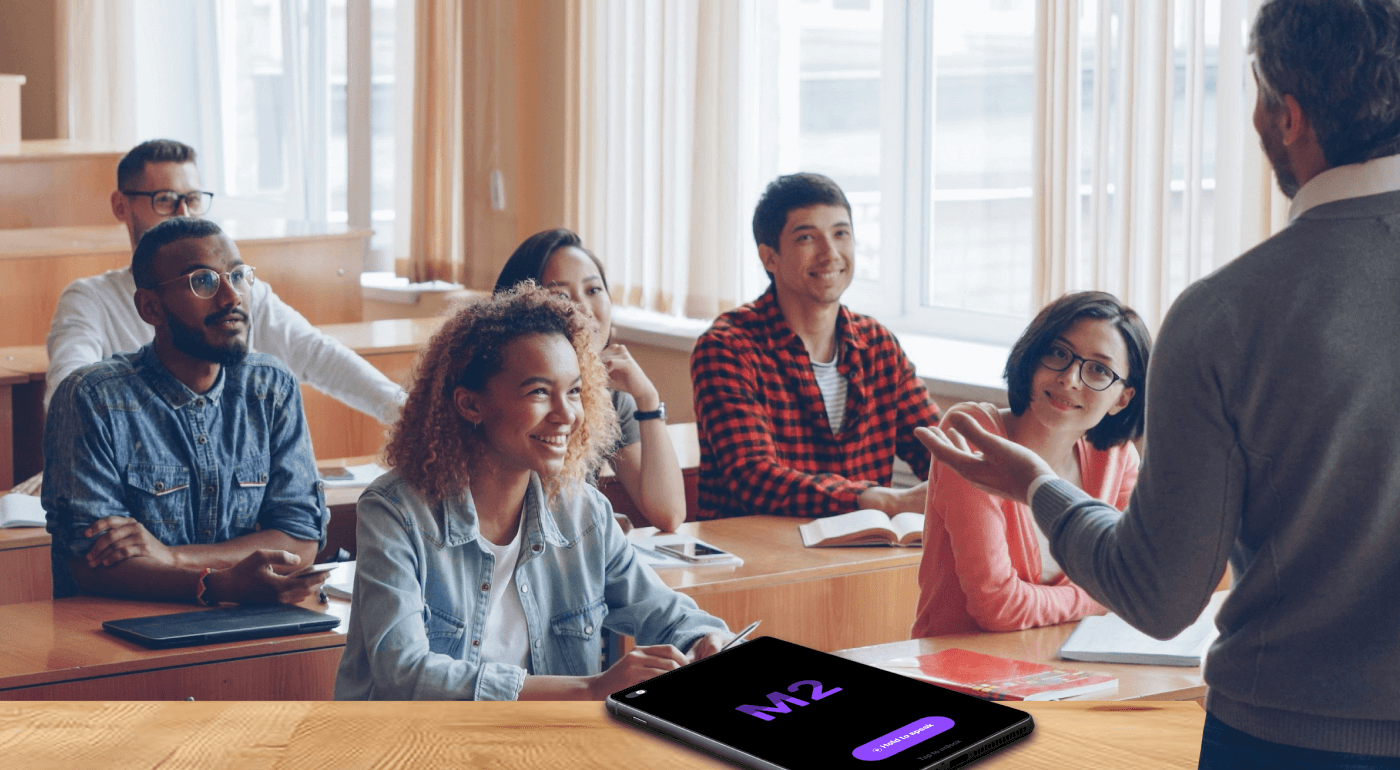 Teacher engaging diverse students in a classroom discussion with the M2 app displayed on a tablet in the foreground